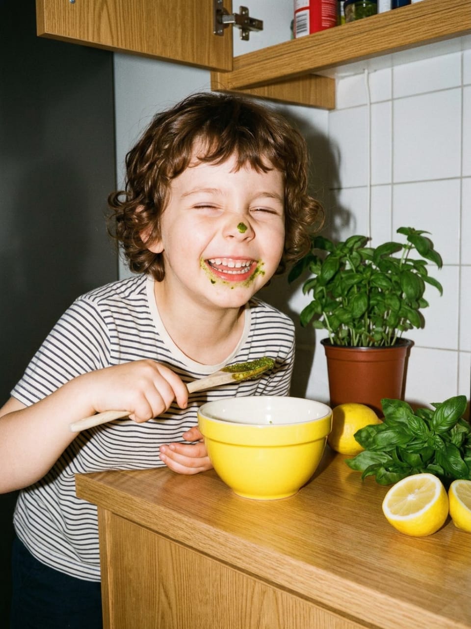 Een kind giechelt met pesto op zijn kin na het proeven
